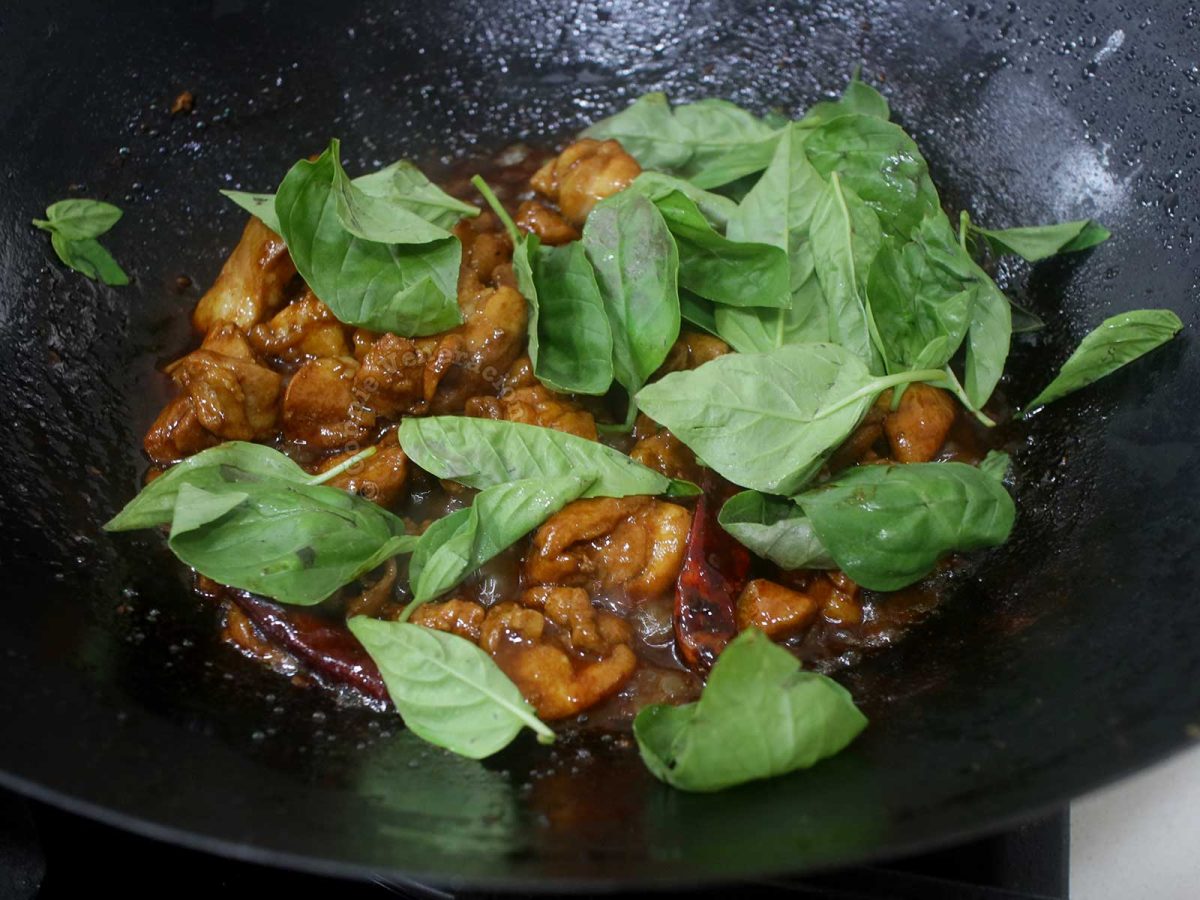 Adding basil leaves to three-cup chicken in wok