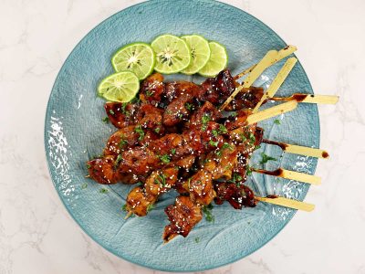 Honey balsamic chicken skewers sprinkled with parsley and toasted sesame seeds, and served with lime slices on the side