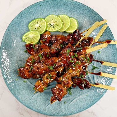 Honey balsamic chicken skewers sprinkled with parsley and toasted sesame seeds, and served with lime slices on the side