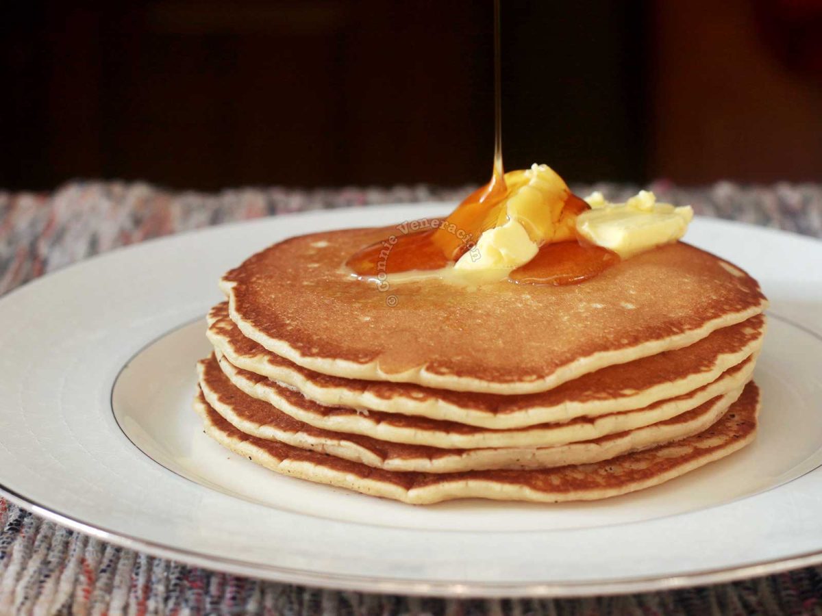 A stack of pancakes, made from scratch, topped with butter and drizzled with honey