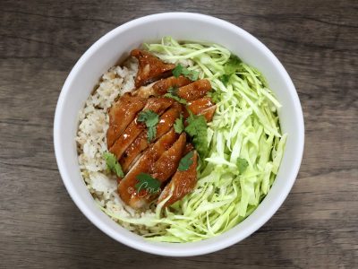 Chicken adobo and shredded cabbage over rice in white bowl