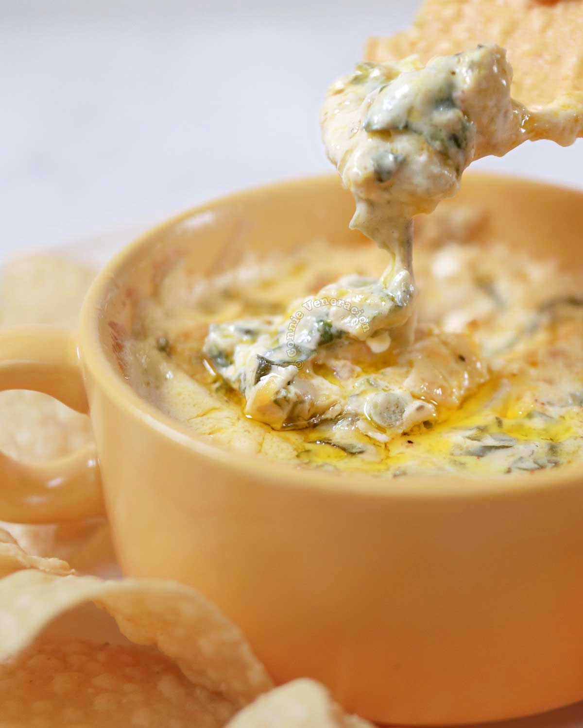 Scooping spinach artichoke dip with tortilla chip