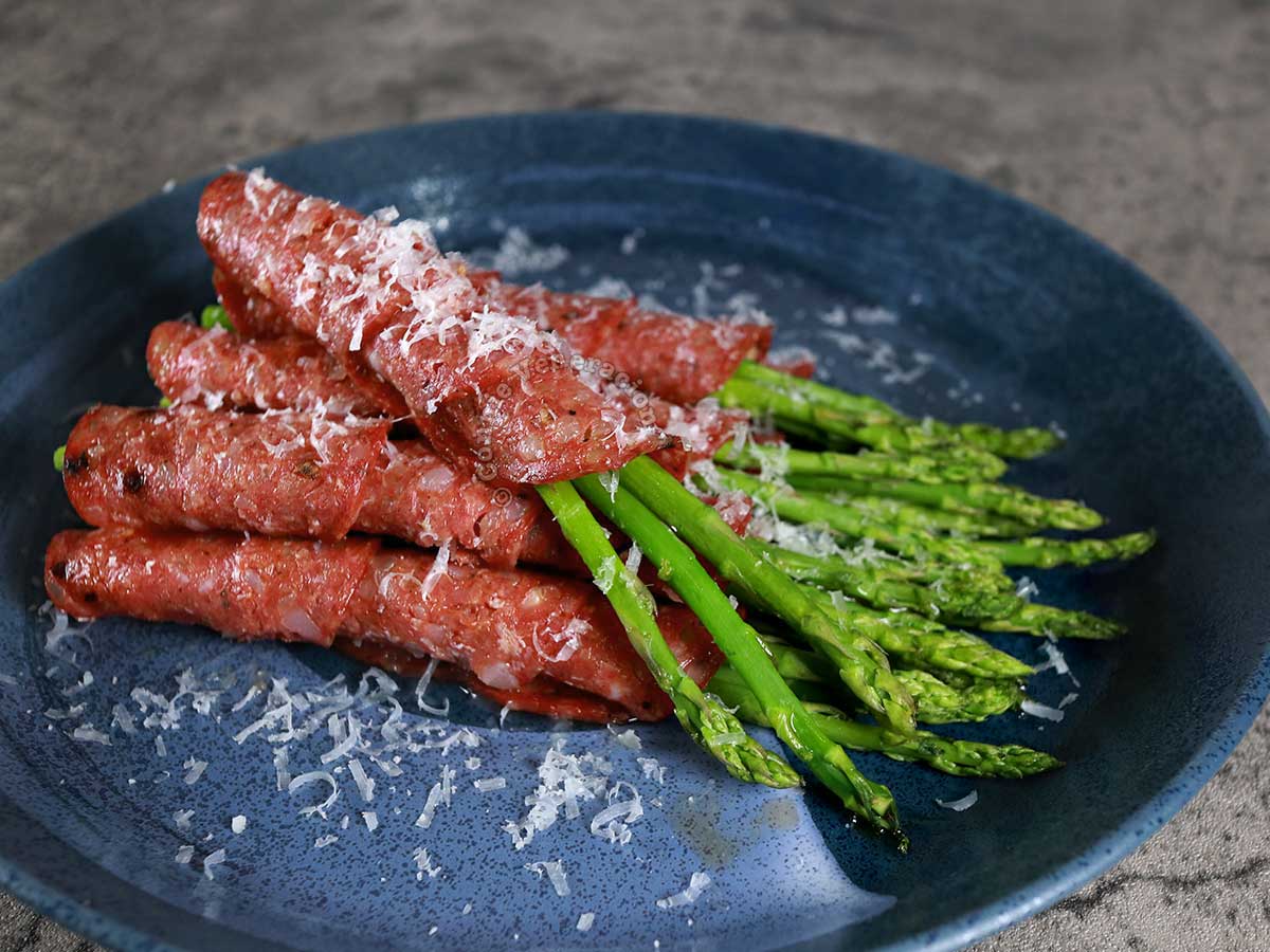 Roasted salami-wrapped asparagus spears garnished with grated Pecorino