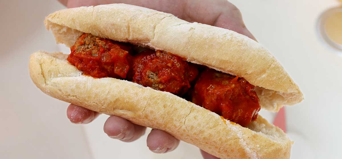 A split baguette stuffed with meatballs in tomato sauce