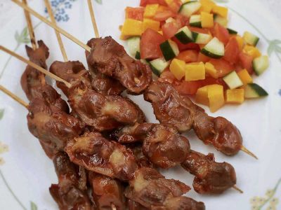 Inihaw na balon-balonan ng manok (skewered and grilled chicken gizzards) on plate with side salad of tomatoes, cucumbers and mangoes