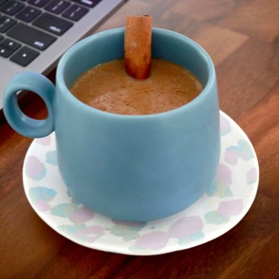 Coffee with cinnamon stick in blue mag; Macbook Pro in the background