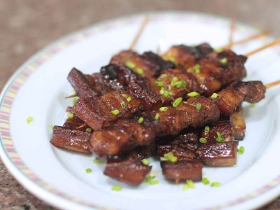 Skewered and grilled Filipino pork adobo garnished with sliced scallions