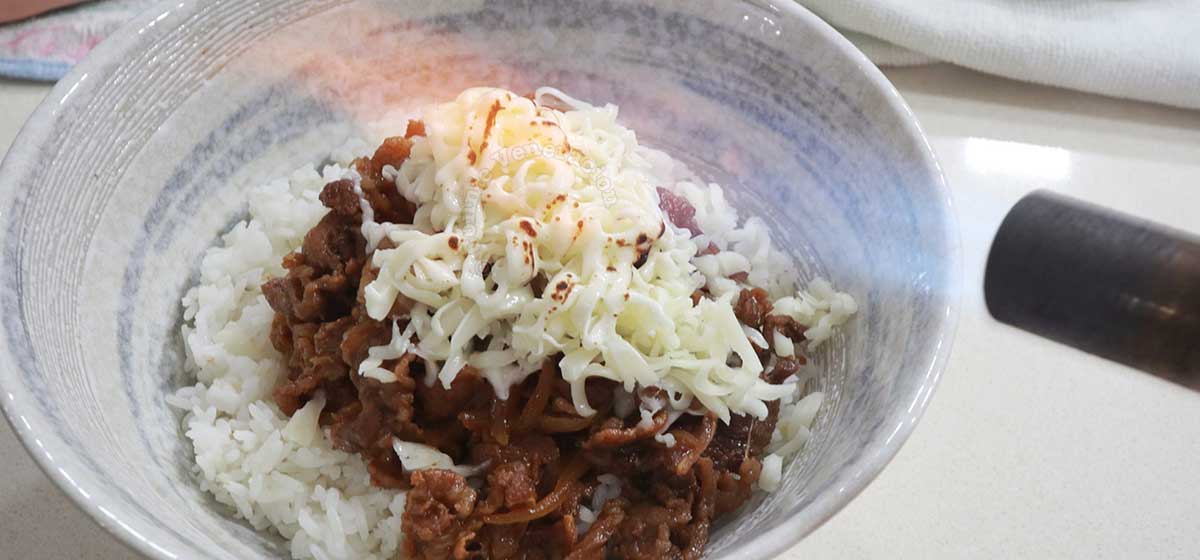 Melting grated cheese on top of gyudon with kitchen torch
