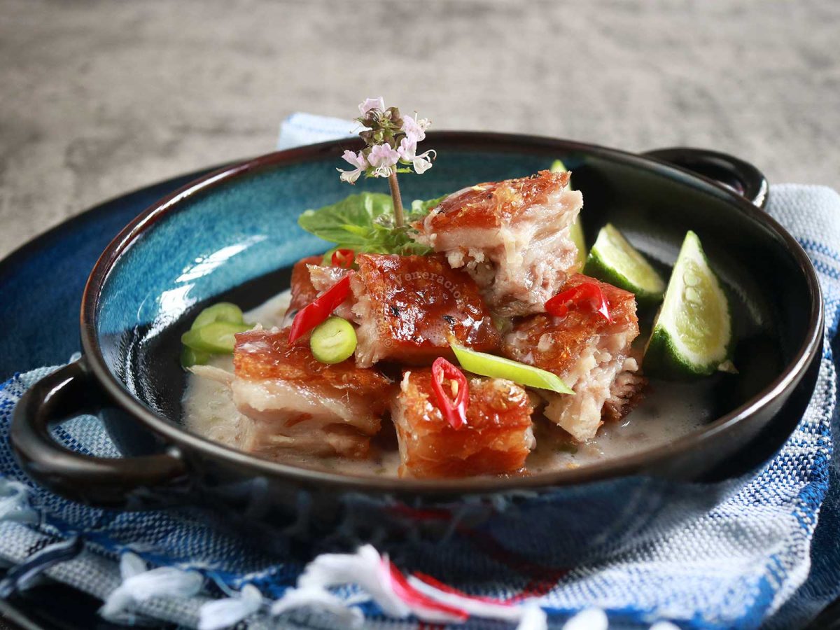 Crispy pork belly in coconut cream sauce garnished with slices of red and green chilies