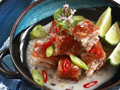 Crispy pork belly in coconut cream sauce garnished with slices of red and green chilies and served with kaffir lime wedges on the side