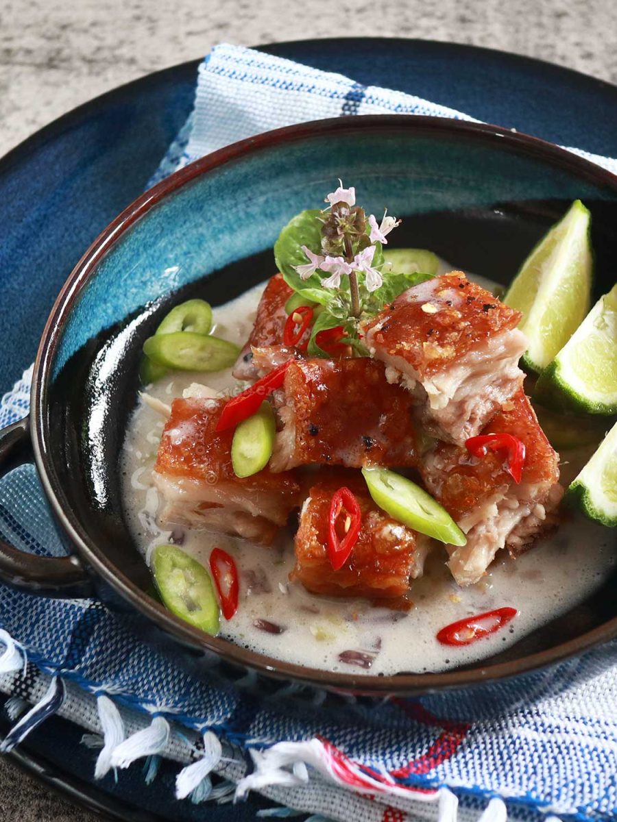 Crispy pork belly in coconut cream sauce garnished with slices of red and green chilies and served with kaffir lime wedges on the side