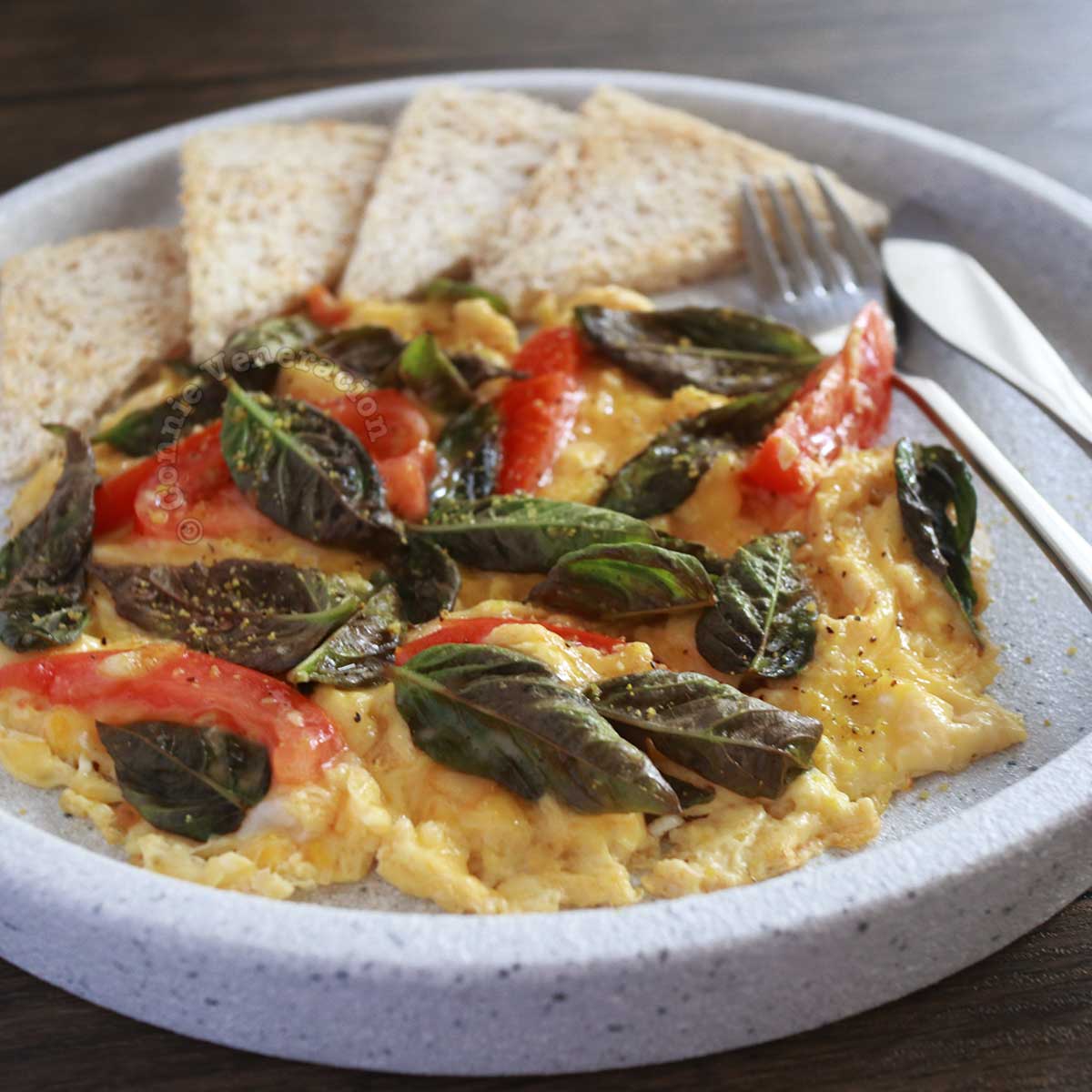 scrambled eggs with tomato, basil and cheese, served with bread on the side