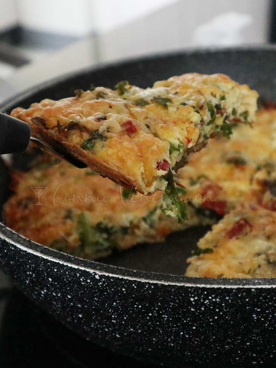 Lifting a wedge of cheesy kale and salami frittata from the pan