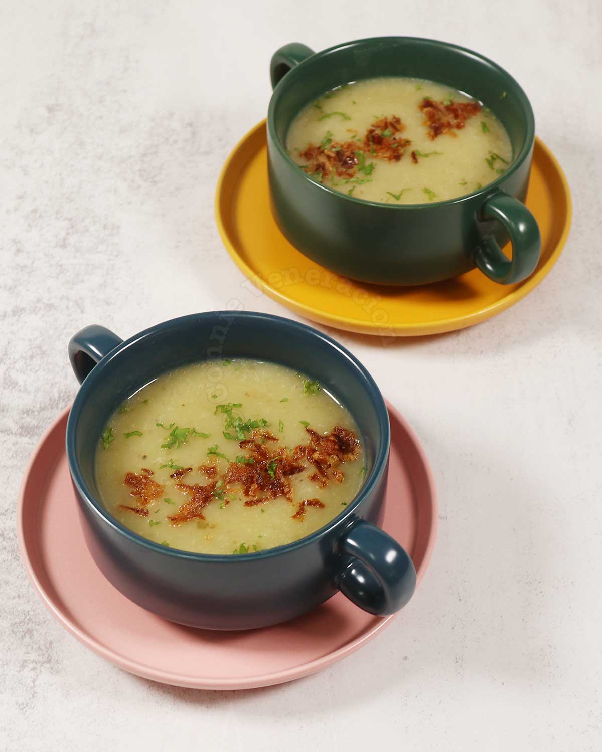 Two bowls of Pureed leeks and potato soup garnished with fried shallots
