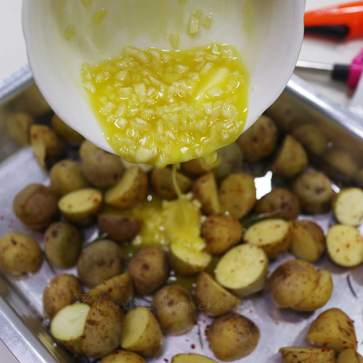 Pouring melted butter and garlic over halved baby potatoes in baking tray
