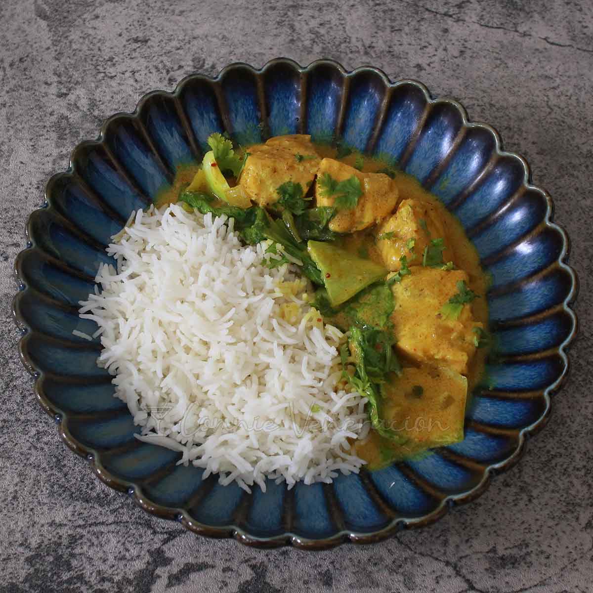 Salmon curry with bok choy and rice in dark blue shallow bowl