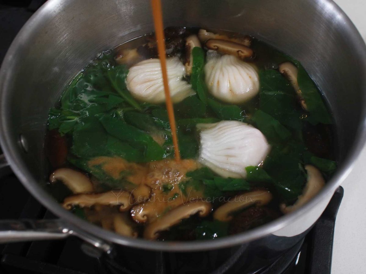Pouring diluted miso into pot with spinach, shrimp wontons and shiitake