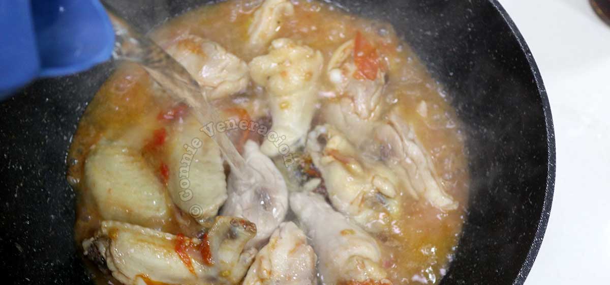 Pouring water into pan with chicken and vegetables