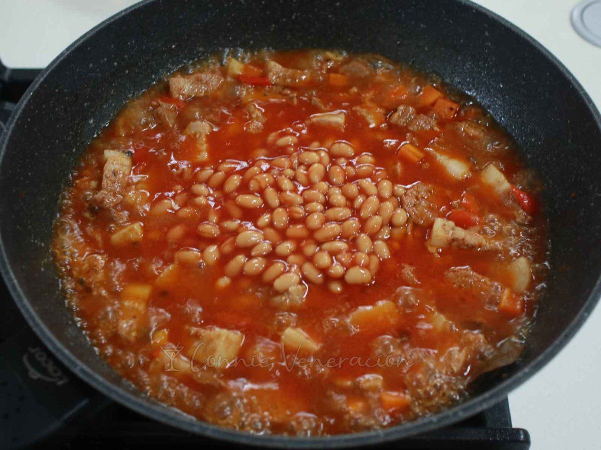 Adding beans to pork and sausage in pan