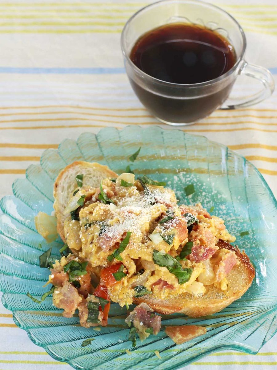 Scrambled eggs with bacon and tomatoes served over s slice of bread