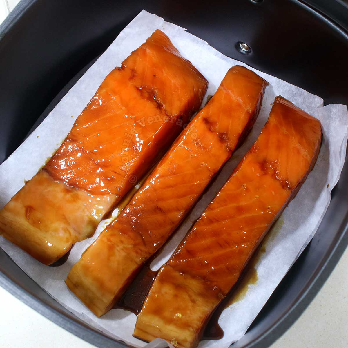 Arranging marinated salmon fillets in air fryer basket lined with parchment paper