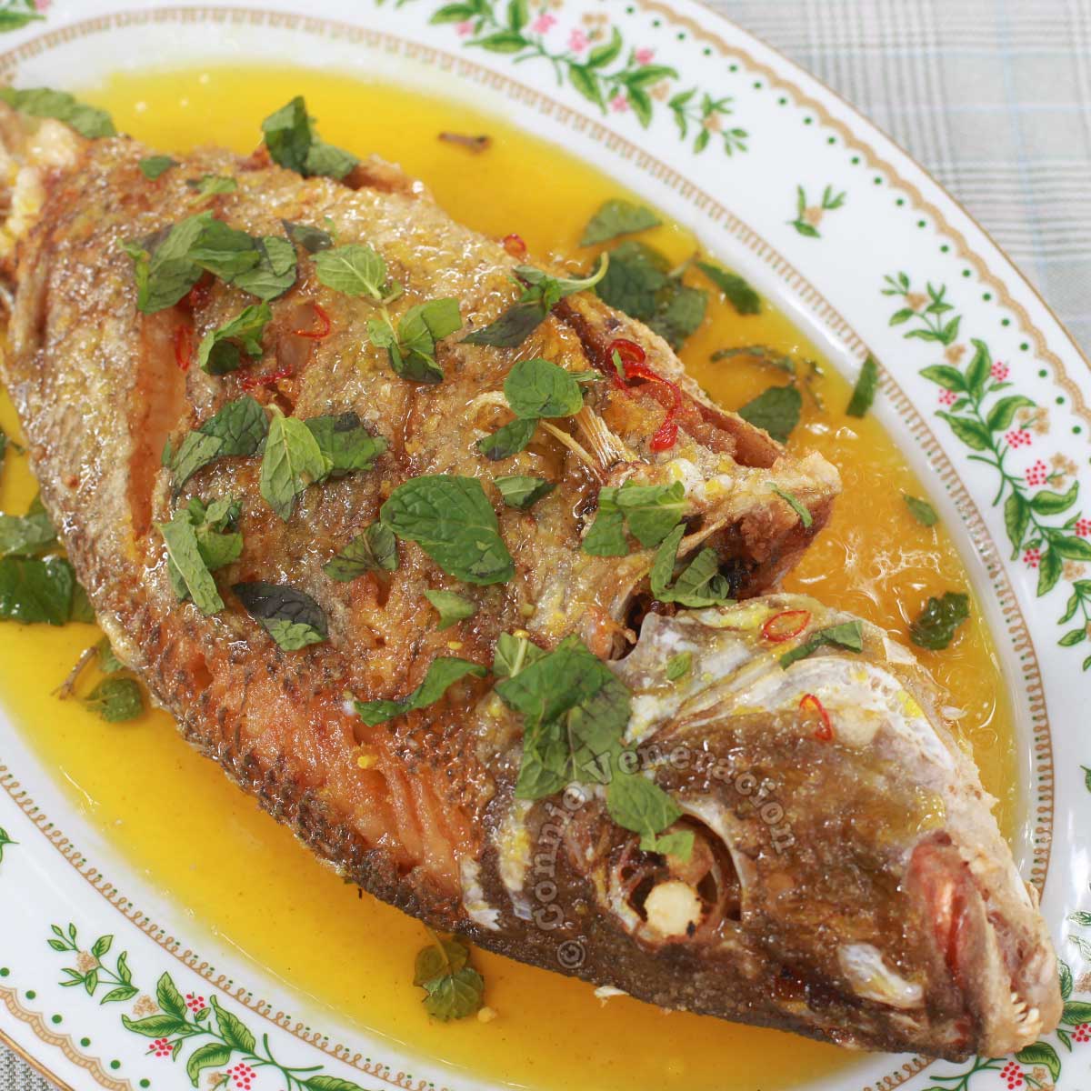 Fried whole fish with lemon sauce garnished with mint leaves