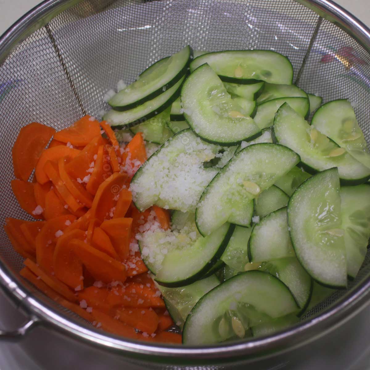Sliced carrot and cucumber sprinkled with salt in colander