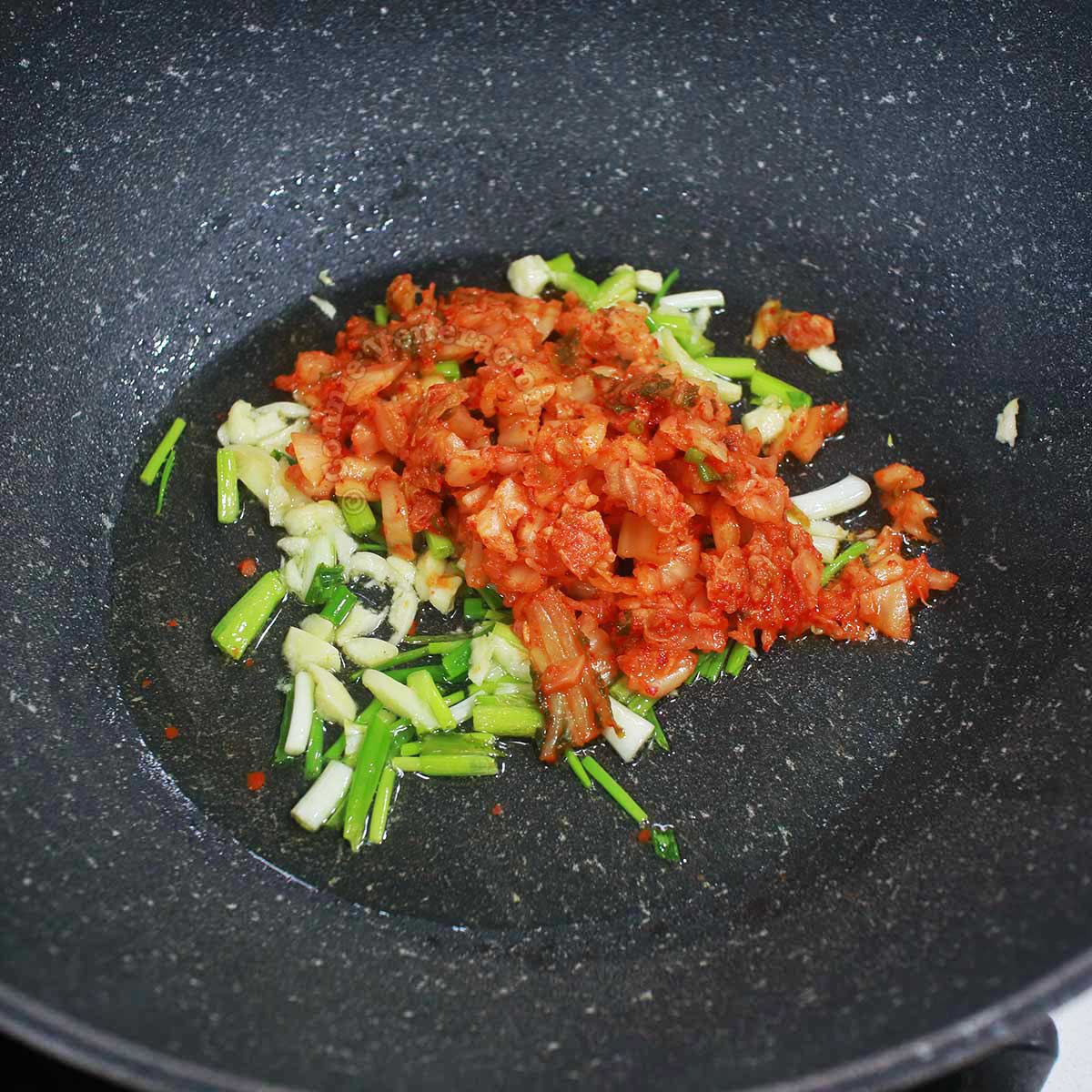 Adding chopped kimchi to sauteed scallions and garlic