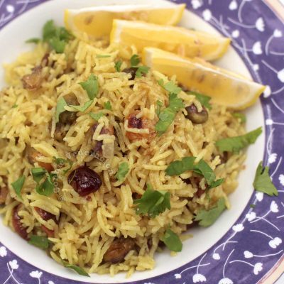 Cranberry and pistachio pilaf garnished with cilantro and served with lemon wedges on the side