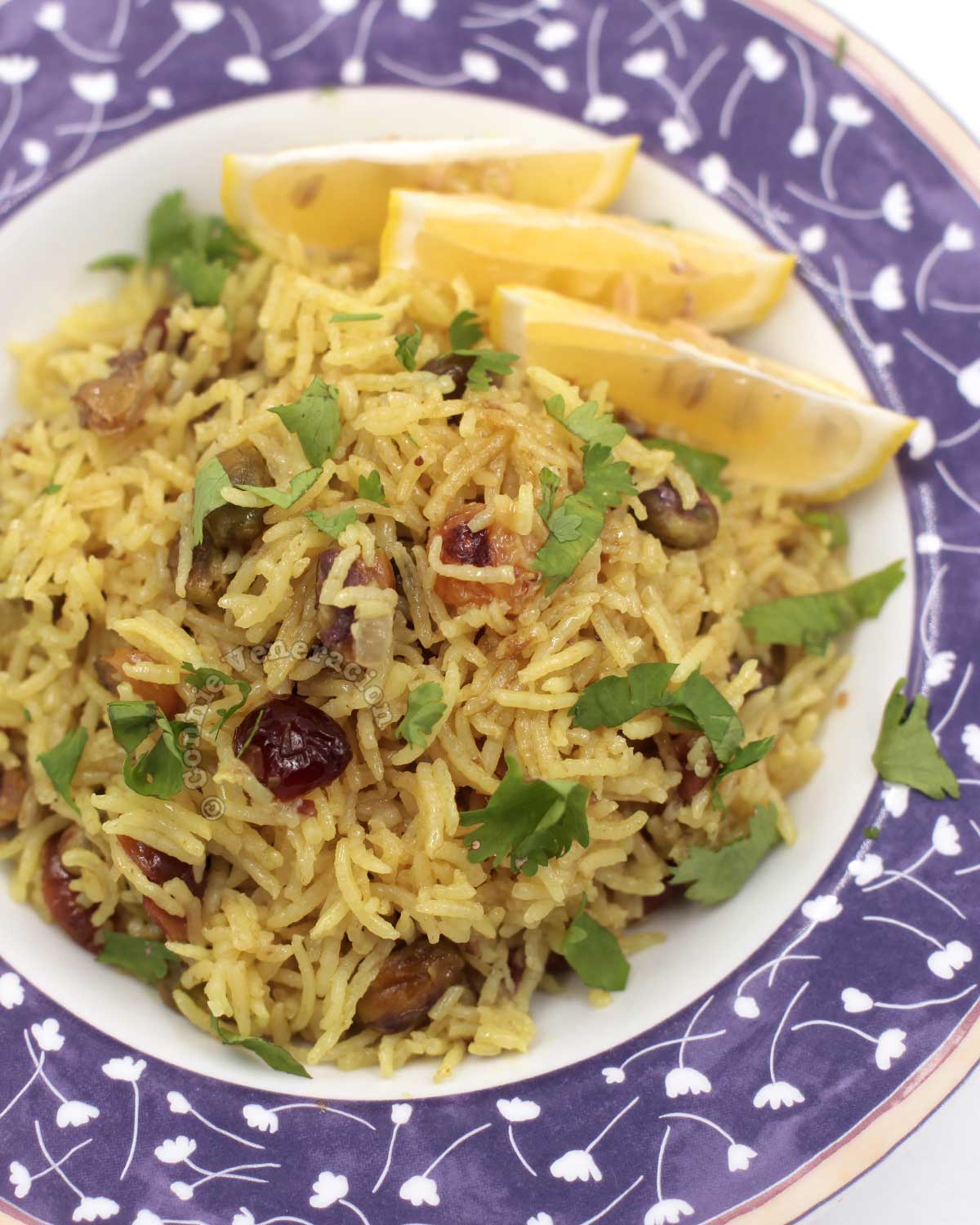 Cranberry and pistachio pilaf garnished with cilantro and served with lemon wedges on the side