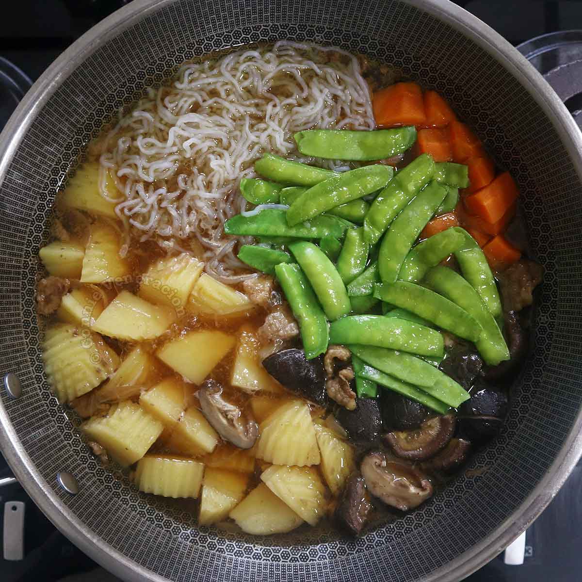 Adding potatoes, shiratake, peas, carrot and shiitake to beef in pan