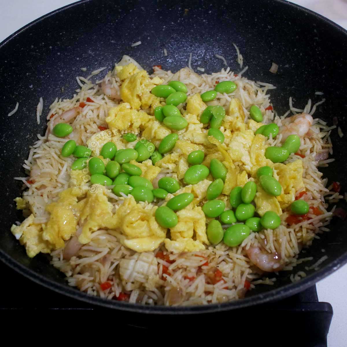 Adding scrambled egg and edamame to shrimp and squid fried rice in wok