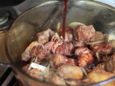 Pouring red wine into pot with beef