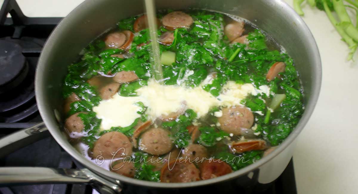 Pouring cream into pot with kale, sausage and potato soup