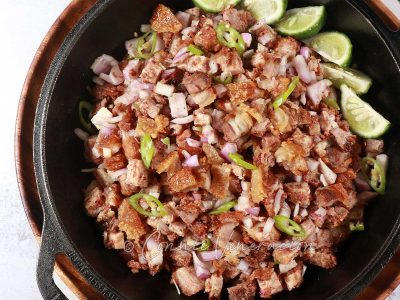 Crispy pork belly sisig with lime wedges in cast iron pan