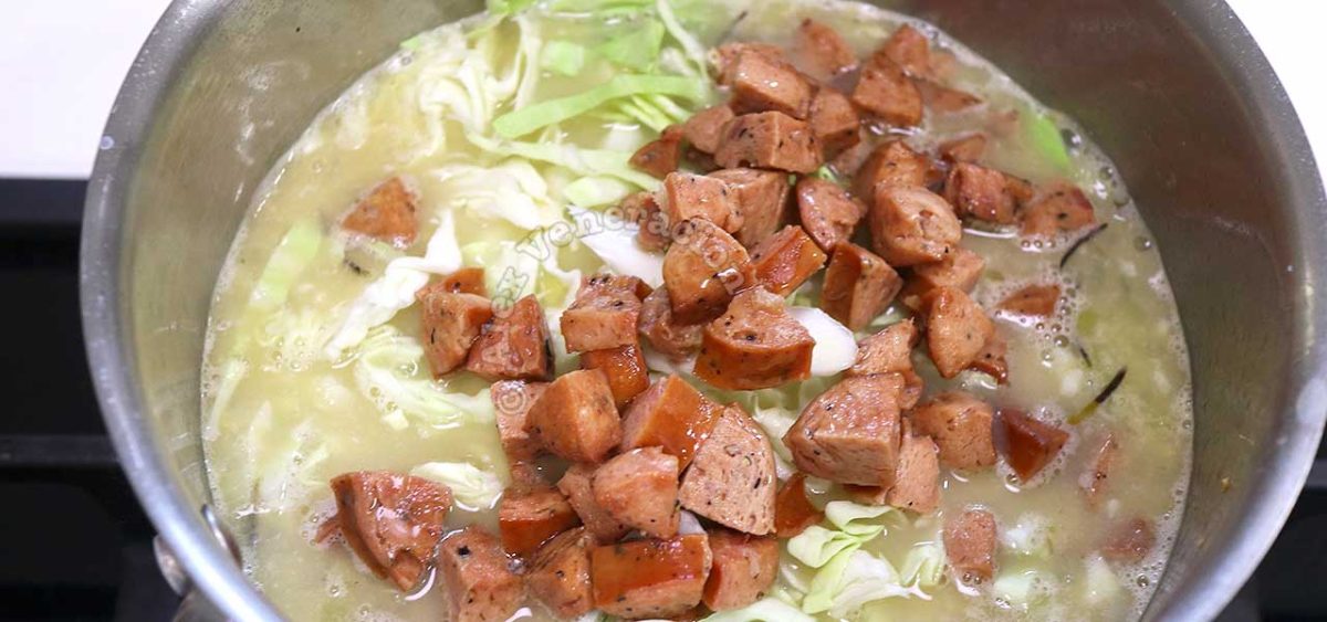 Adding browned sausages to chickpeas and cabbage in pot