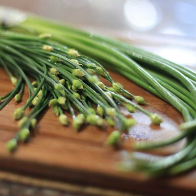 Garlic chives and garlic scapes on bamboo chopping board