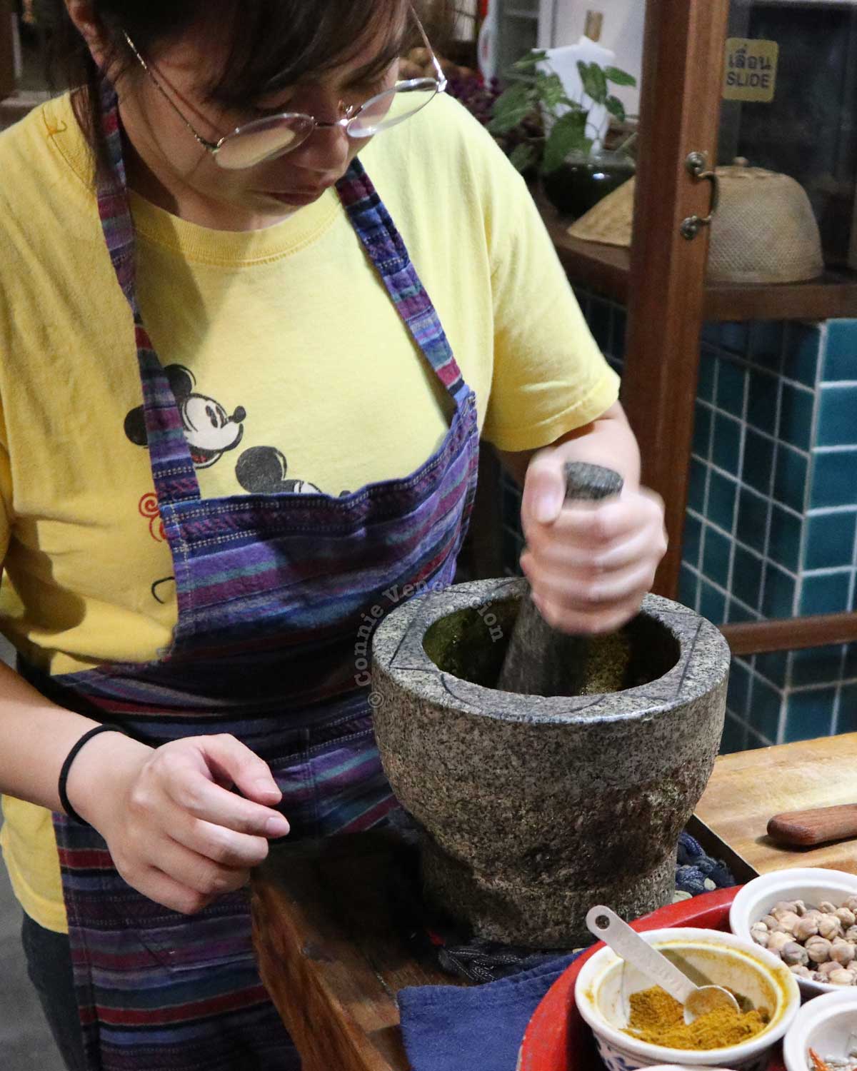 Grinding spices and herbs with an mortar and pestle made of unpolished granite. Chiang Mai, Thailand, 2020