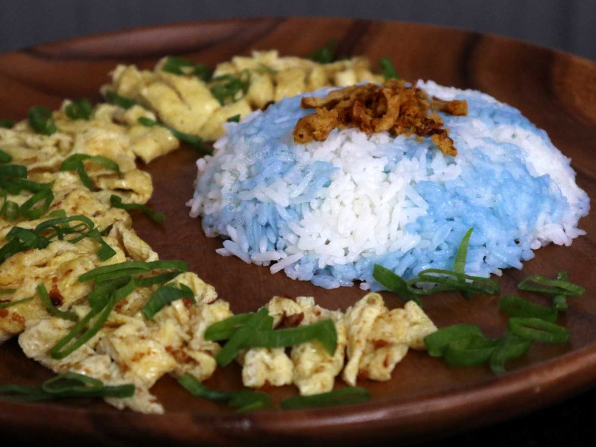 Malaysian butterfly pea flower rice (nasi kerabu) with sliced omelette on wooden plate