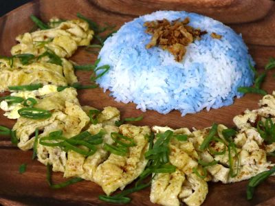 Malaysian butterfly pea flower rice (nasi kerabu) with sliced omelette on wooden plate