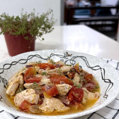 Chicken, tomatoes and thyme in olive oil, with pot of thyme in background