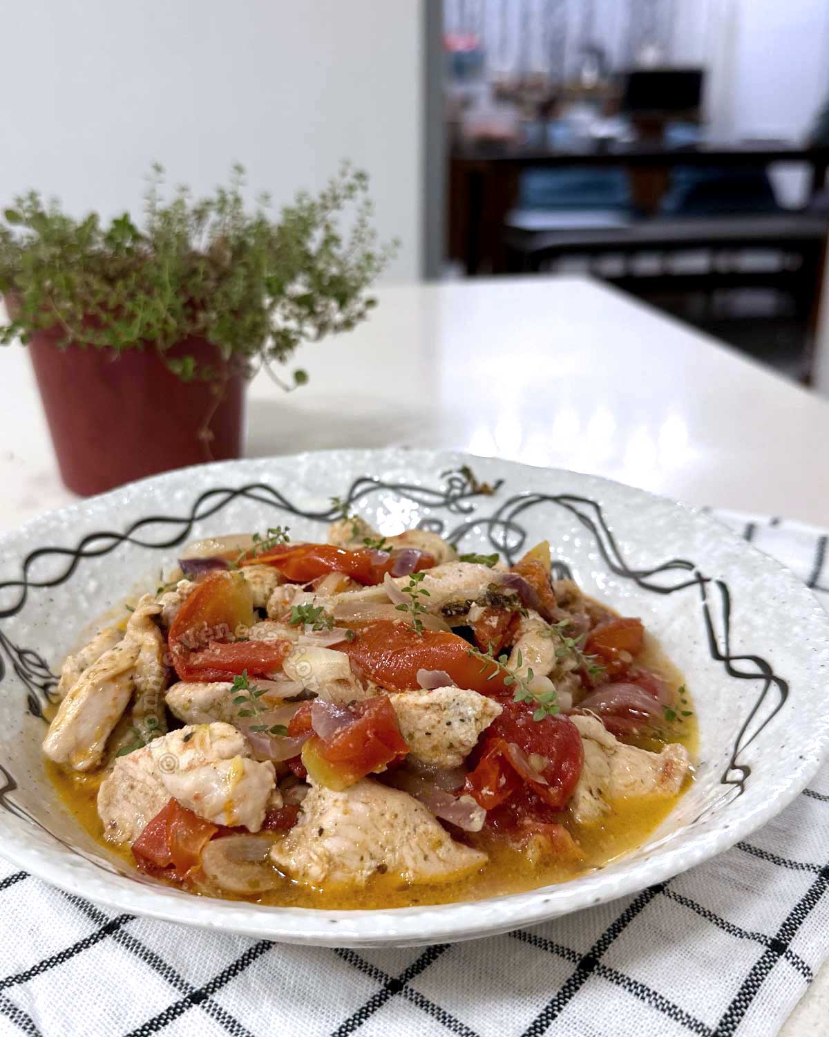 Chicken, tomatoes and thyme in olive oil, with pot of thyme in background