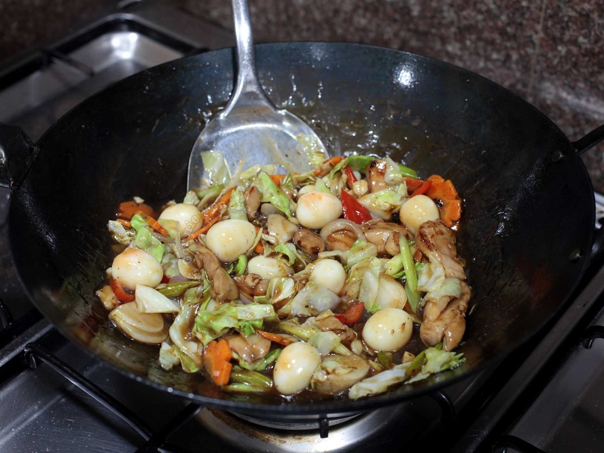 Stir frying chicken, vegetables and quail eggs in carbon steel wok