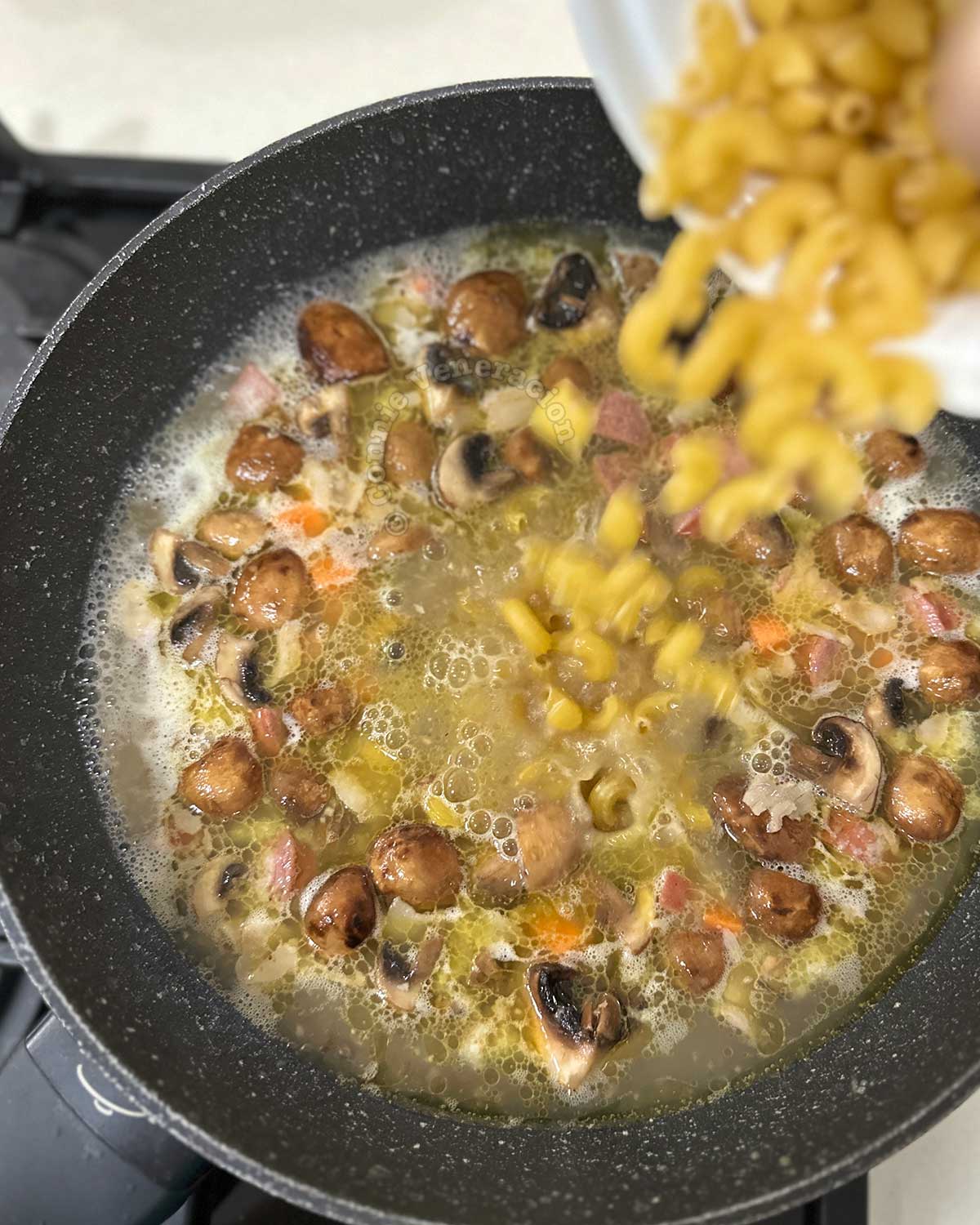 Adding elbow macaroni to soup in pan