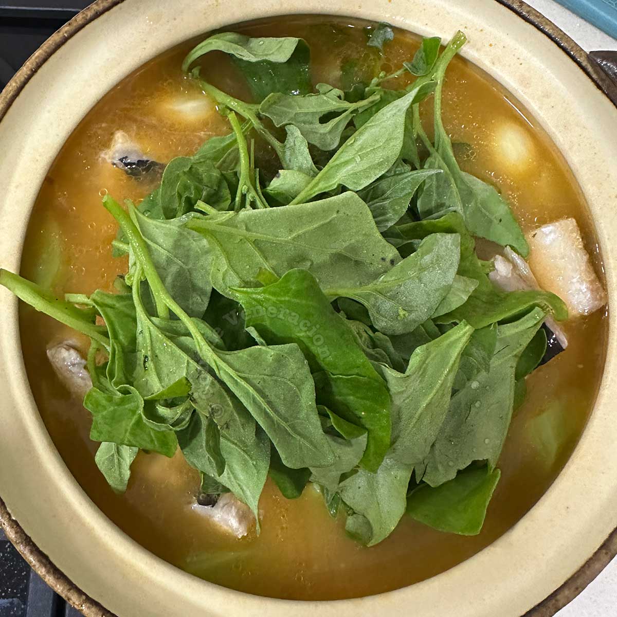 Adding spinach to fish soup in claypot