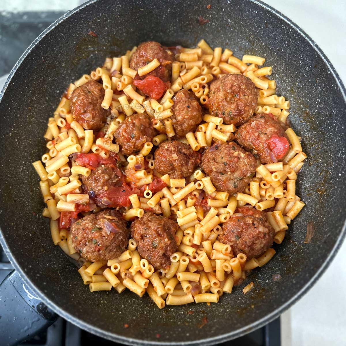 Cooked macaroni and meatballs in tomato sauce in wok