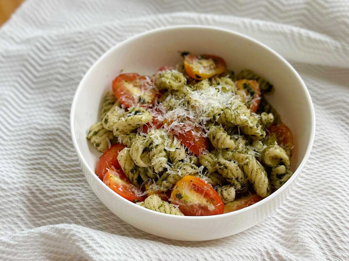 Homemade pasta with pesto and cheery tomatoes topped with grated Pecorino